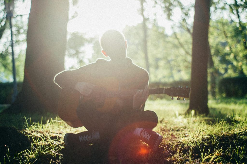 man siting on grass while playing guitar