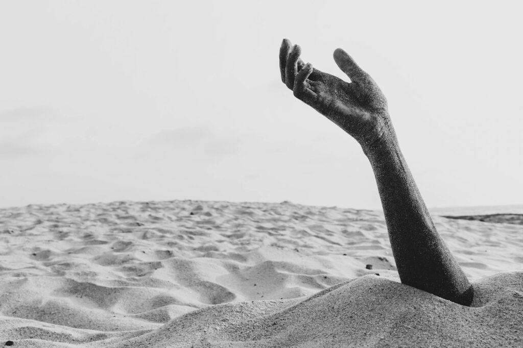 hand of man buried in sand on beach