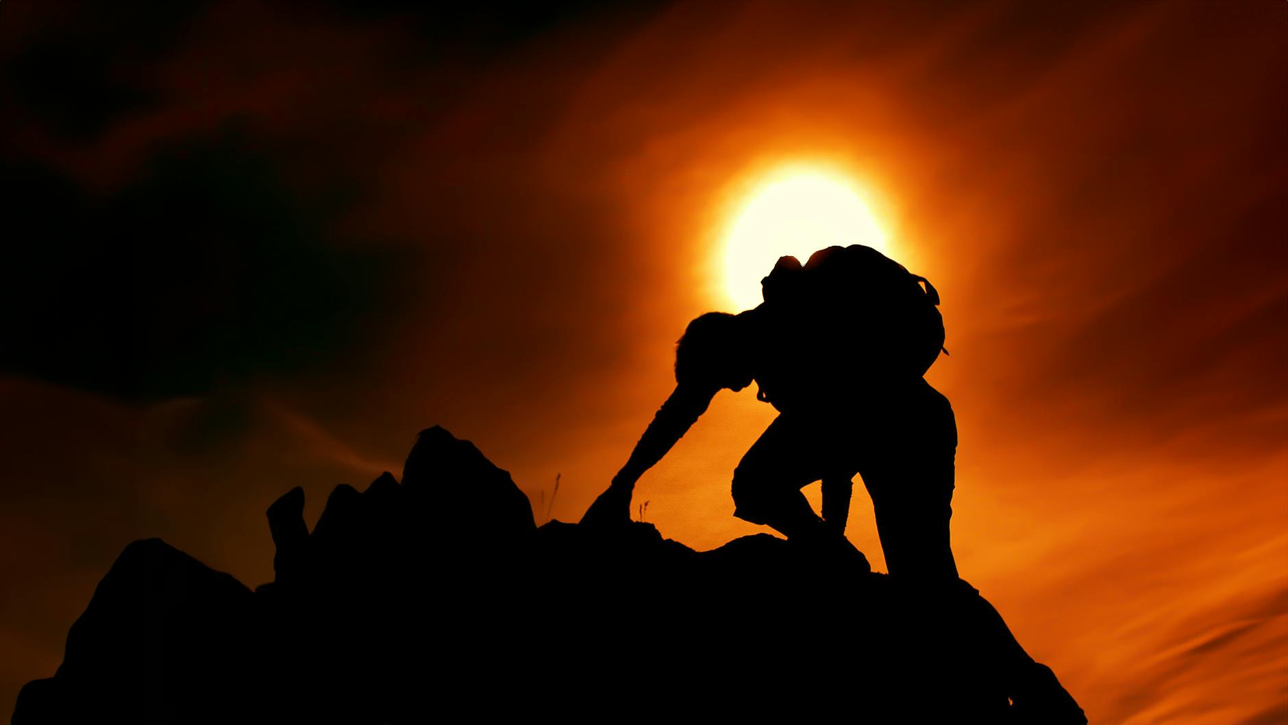 sun over silhouette of man rock climbing
